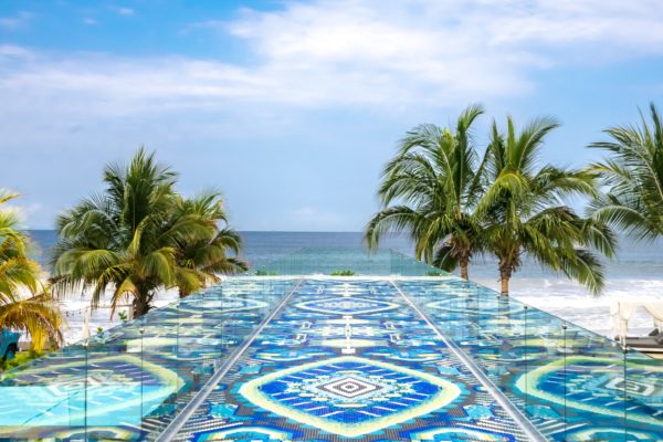 a glass walkway with palm trees and a beach